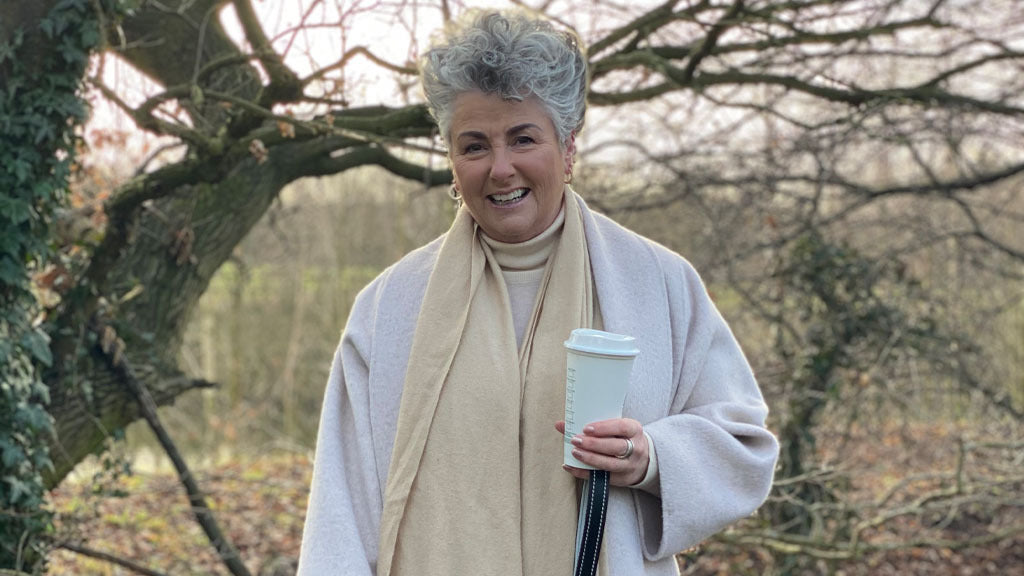 Foto von Maxine Laceby die draußen steht, einen Kaffee in der Hand hat und lächelt